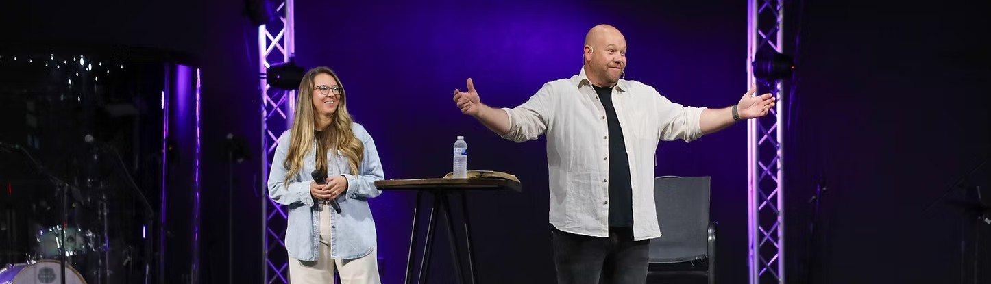 Pastor Brian Loudermilk on stage with his arms open wide, with his wife, Mandee